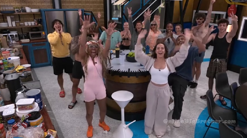 Big Brother houseguests cheering and raising their hands in celebration inside the house kitchen area
