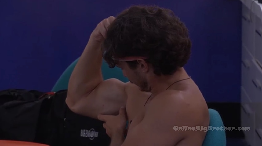 A shirtless Big Brother houseguest sits with his hand on his head, appearing stressed or deep in thought