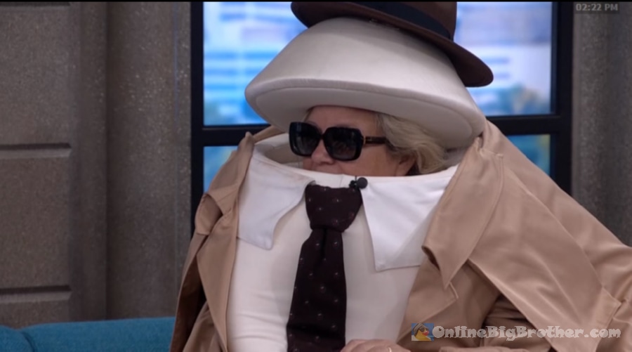 Angela wearing a stacked hat disguise with sunglasses, trench coat, and tie in the Big Brother house at 2:22 pm